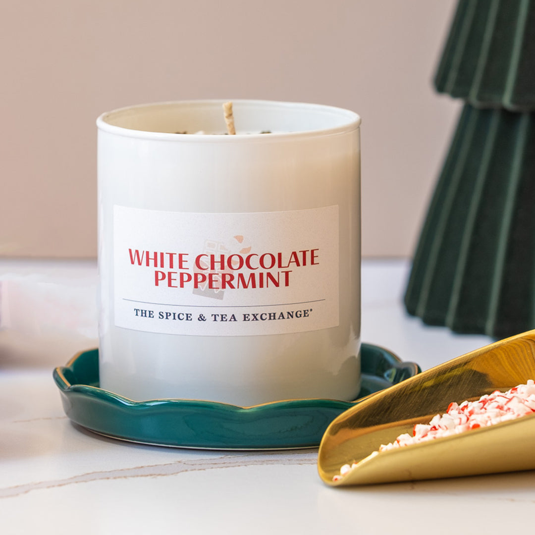 White chocolate peppermint candle with a decorative tray and green tree on a light surface.